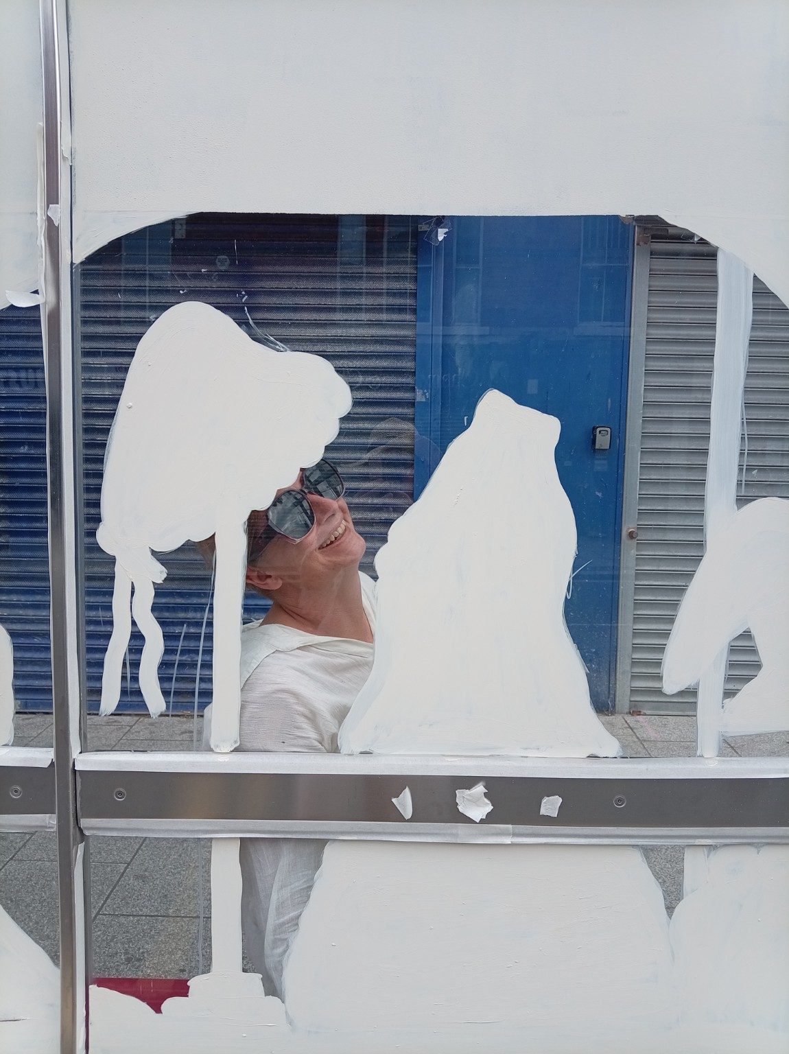 A person smiling through unpainted spaces in a partly painted white bus shelter design