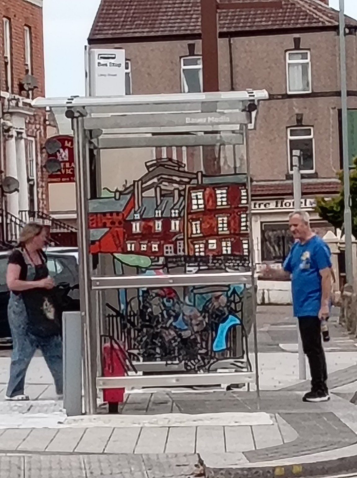 A painted bus shelter seen from across the street with people standing nearby